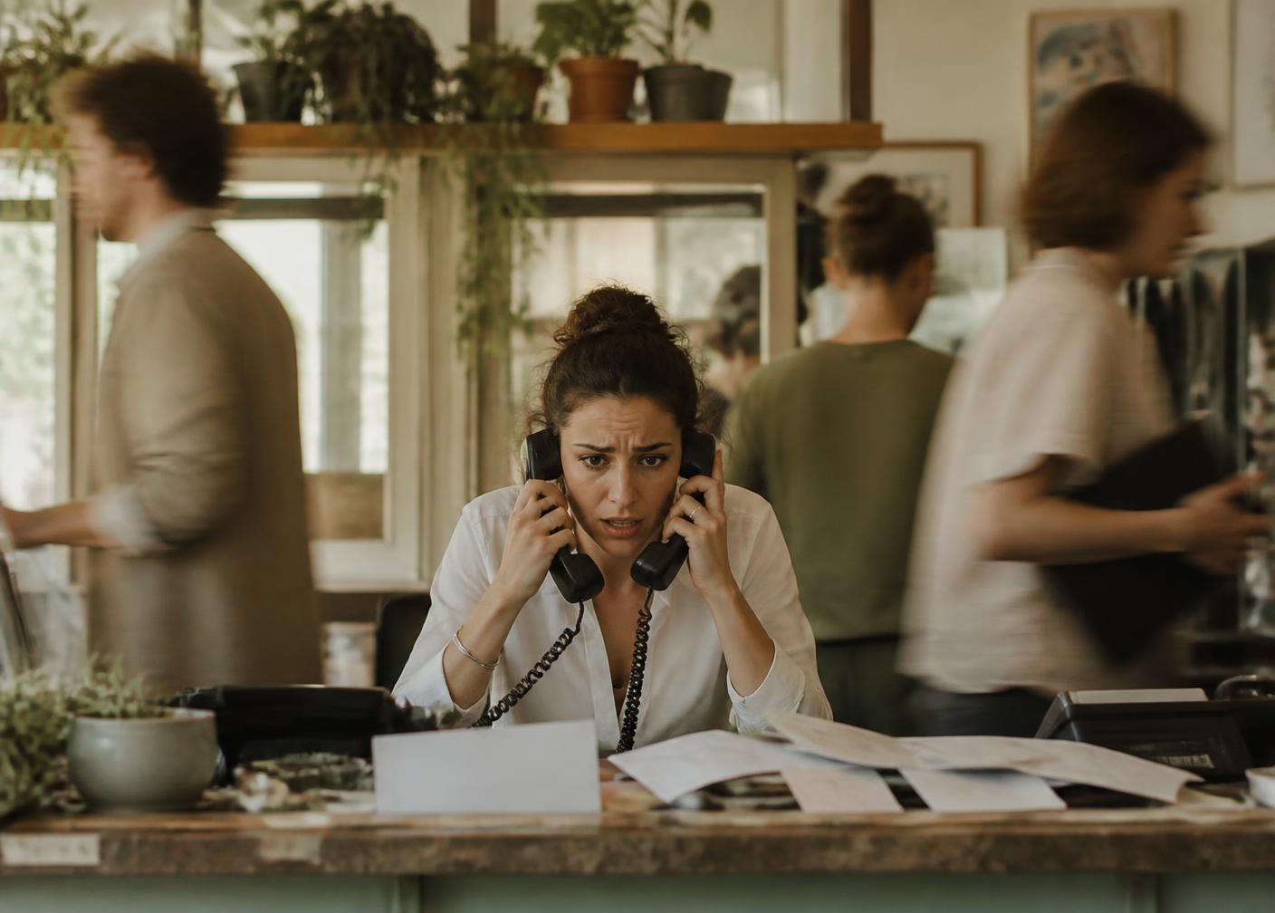 Office manager overwhelmed by phones and paperwork at a busy front desk